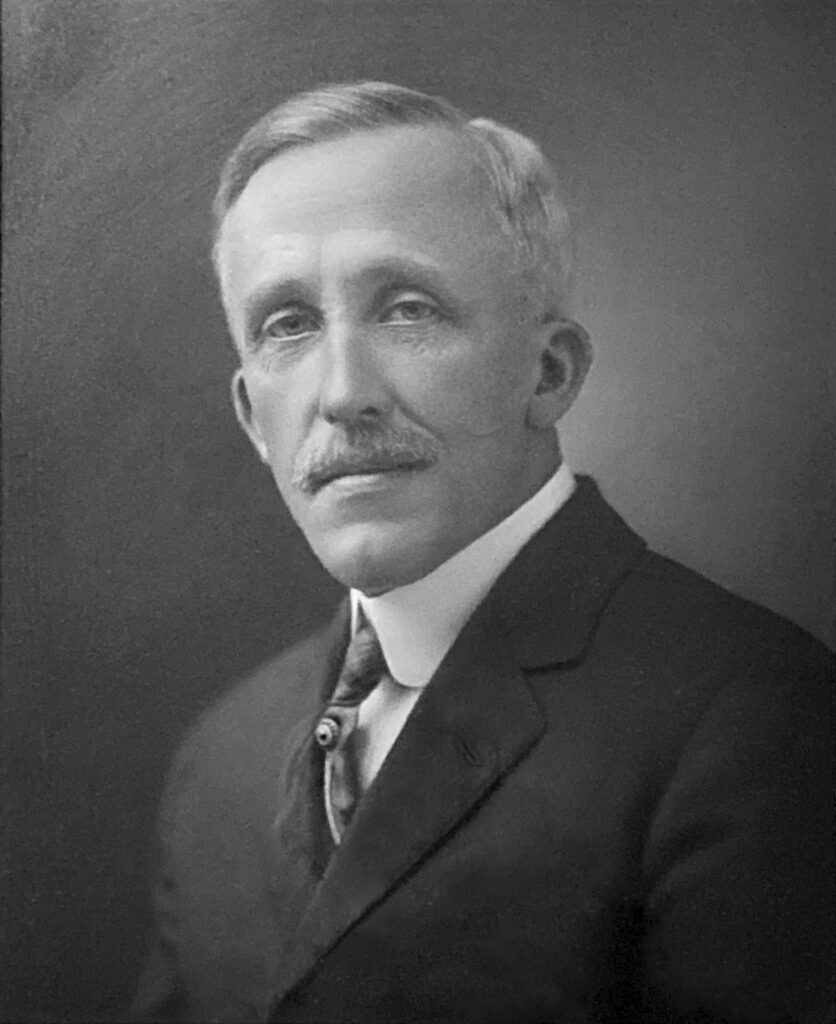 Head and shoulders portrait of a white man with grey hair and a moustache.