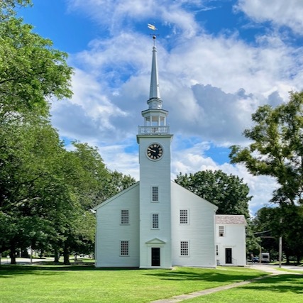 Exterior of wood frame meetinghouse, facing the steeple (short wall), double hung windows, clapboard sides, painted white