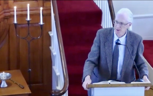 Dan preaching at a lectern, leaning to one side and gesturing