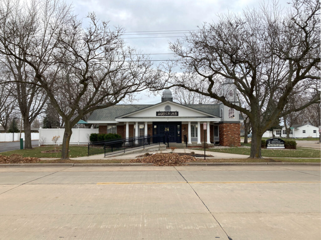 Suburban streetscape, modest one story brick building with white portico and a small minaret on one end.