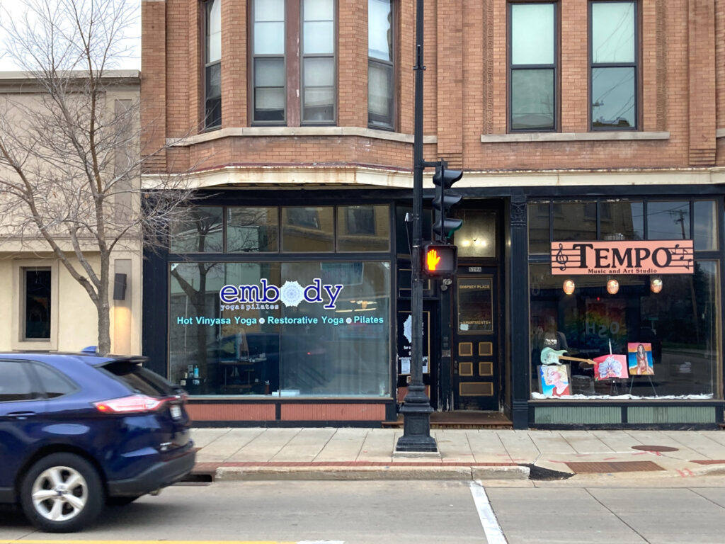 Urban streetscape, two story brick building with two storefronts on the first floor, one of which has a sign for a yoga studio