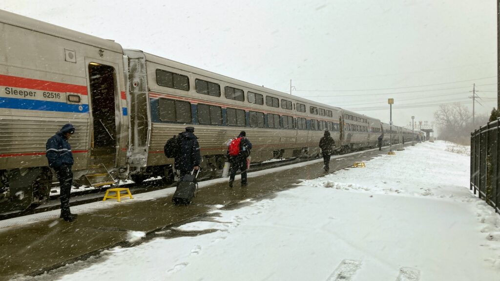 People walking along a stationary train, which stretches into the distance.