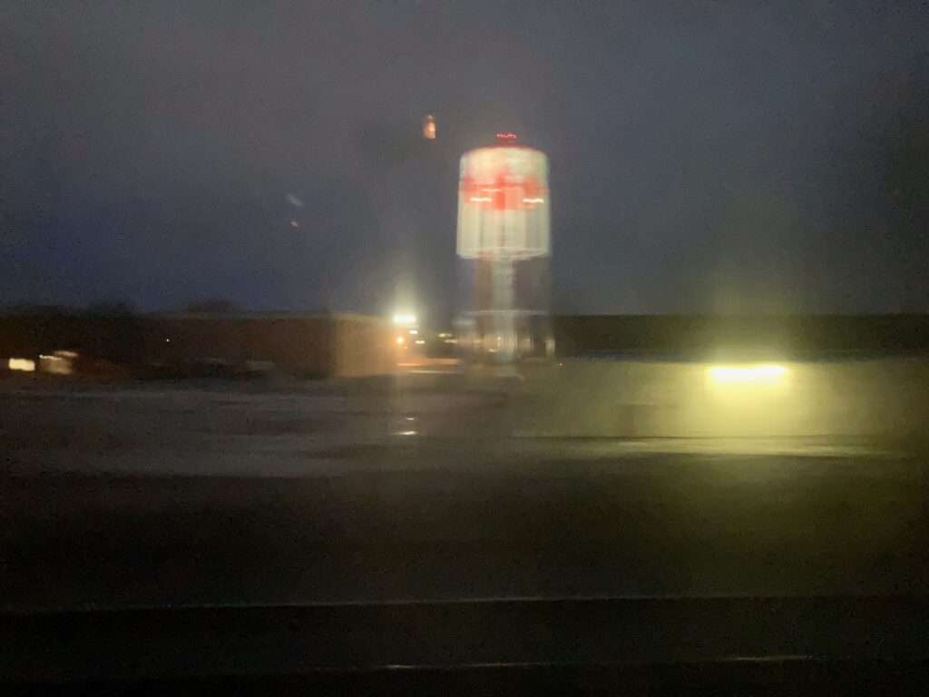 The sky barely turning light, a brightly painted-and blurry sight of a water tower.