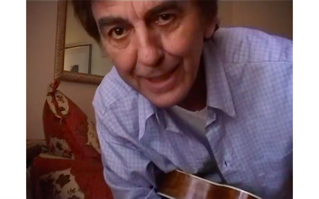 A screen grab from the video of George Harrison playing "I've Got a Shine on My Shoes," showing harrison holding a uke and smiling into the camera.