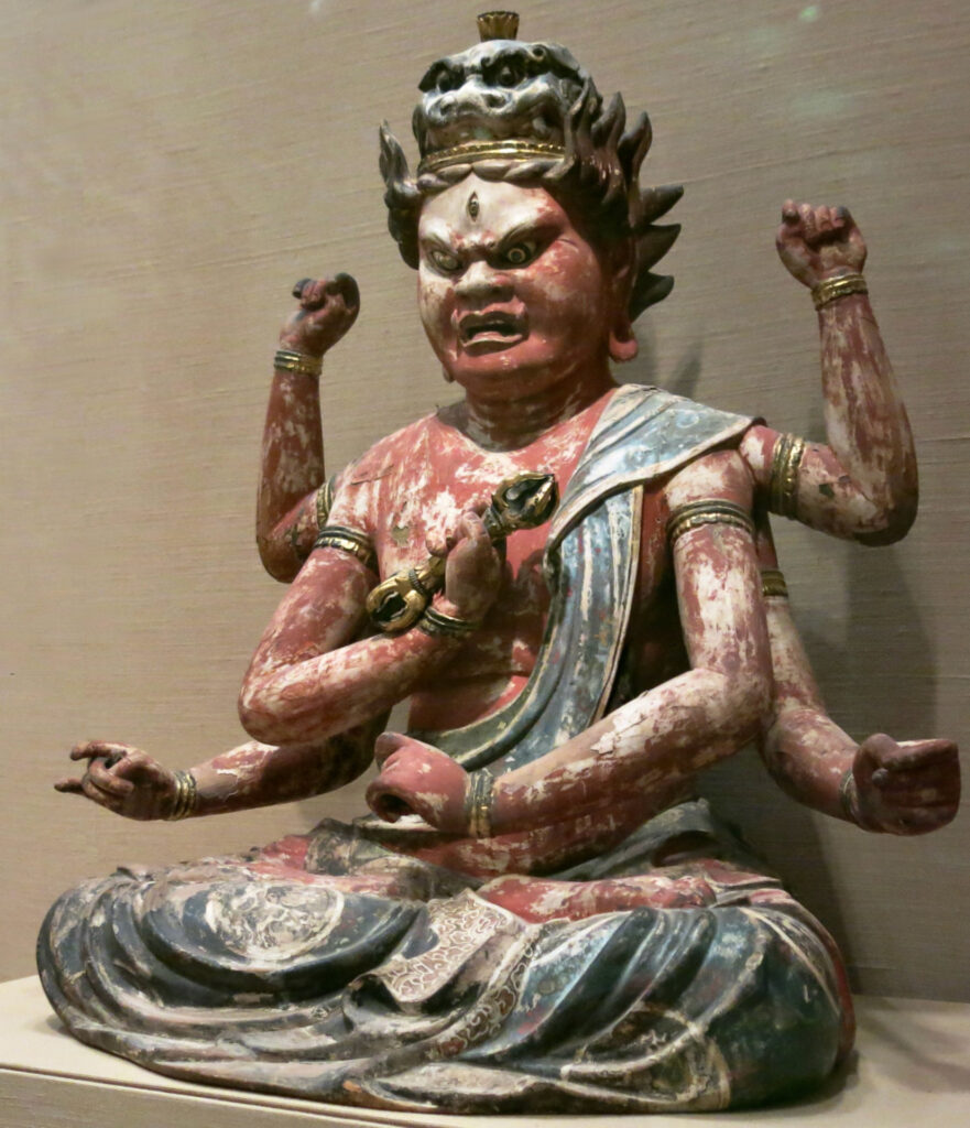 A sculpture of a being with red skin, six arms, and a ferocious expression