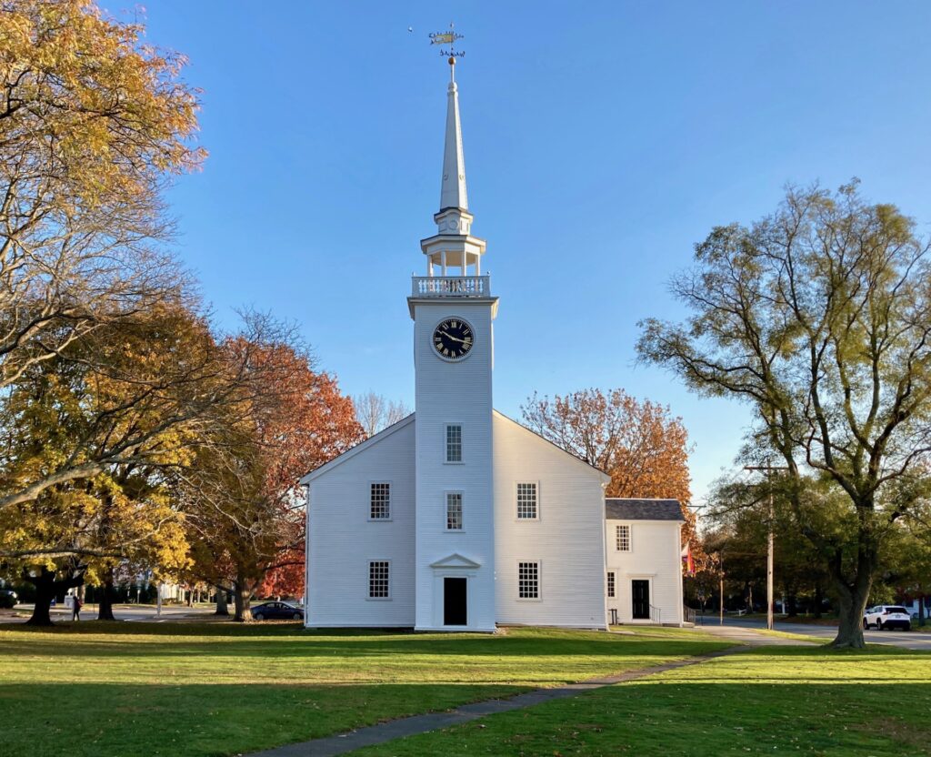 White clapboard New England church set amid lawn and autumnal trees
