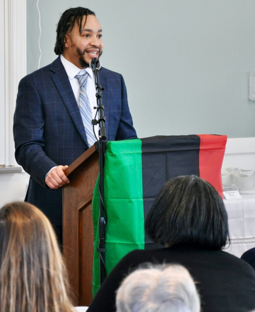 Man standing at a podium draped with the Pan Afrian flag.