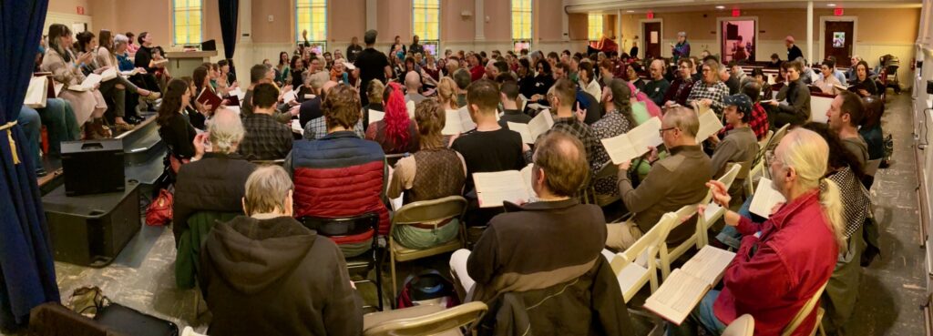 A panoramic view of the singing, with over 150 people visible in the photo.