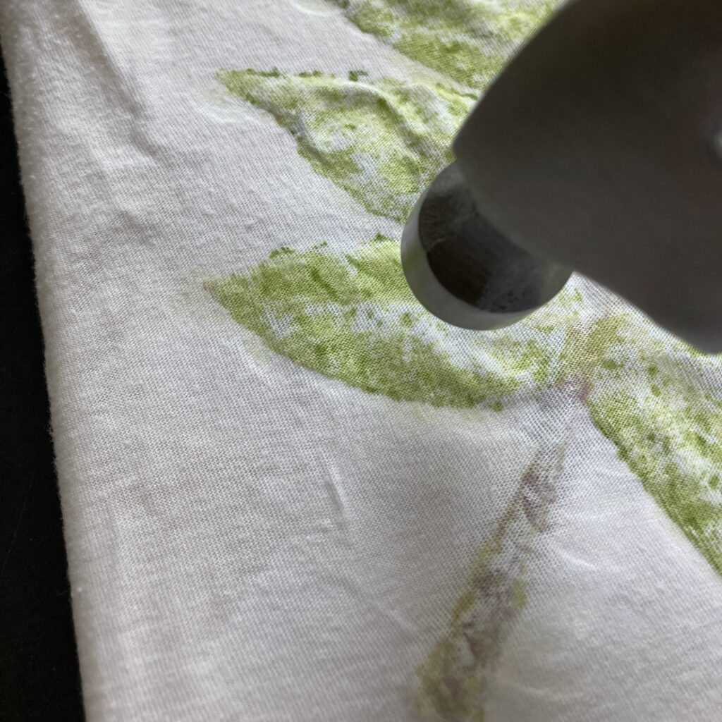 A hammer about to strike a piece of cloth, with outlines of leaves visible in the cloth.