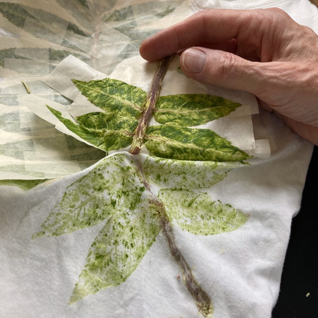 A hand peeling masking tape off the cloth, with hammered leaf material stuck to the tape.